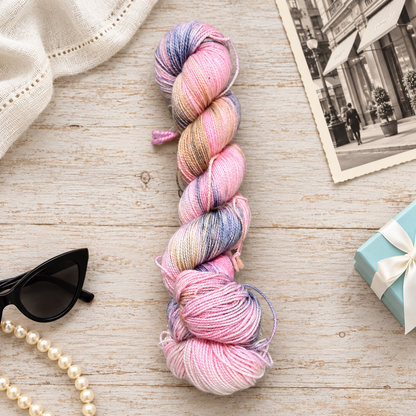 Breakfast at Tiffany’s pink, cream, and lavender-gray hand-dyed yarn with pearls, black sunglasses, a pale blue gift box, and a vintage New York print.