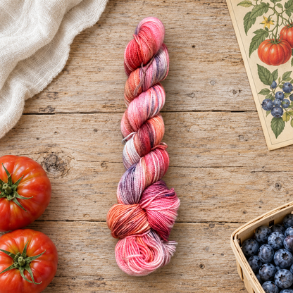 Garden State hand-dyed yarn in tomato red, coral pink, cream, and blueberry purple on rustic wood beside tomatoes, blueberries, and a botanical print.